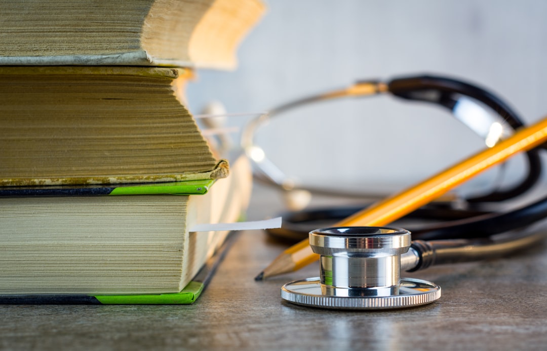 A stack of books next to a stethoscope and a pencil on a desk