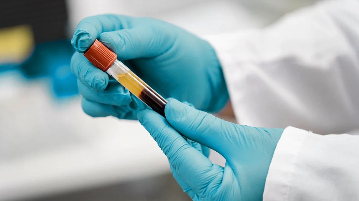 a gloved hand holding a test tube filled with layered liquid samples